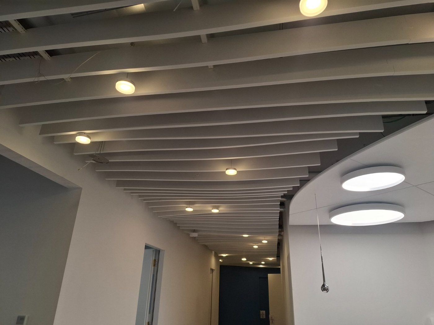 Couloir traité avec baffles acoustiques et luminaires ronds, Bienne